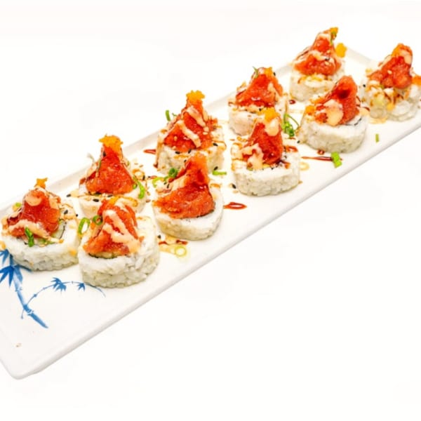 A white rectangular plate with ten sushi rolls topped with spicy tuna, sauce, and green onions.