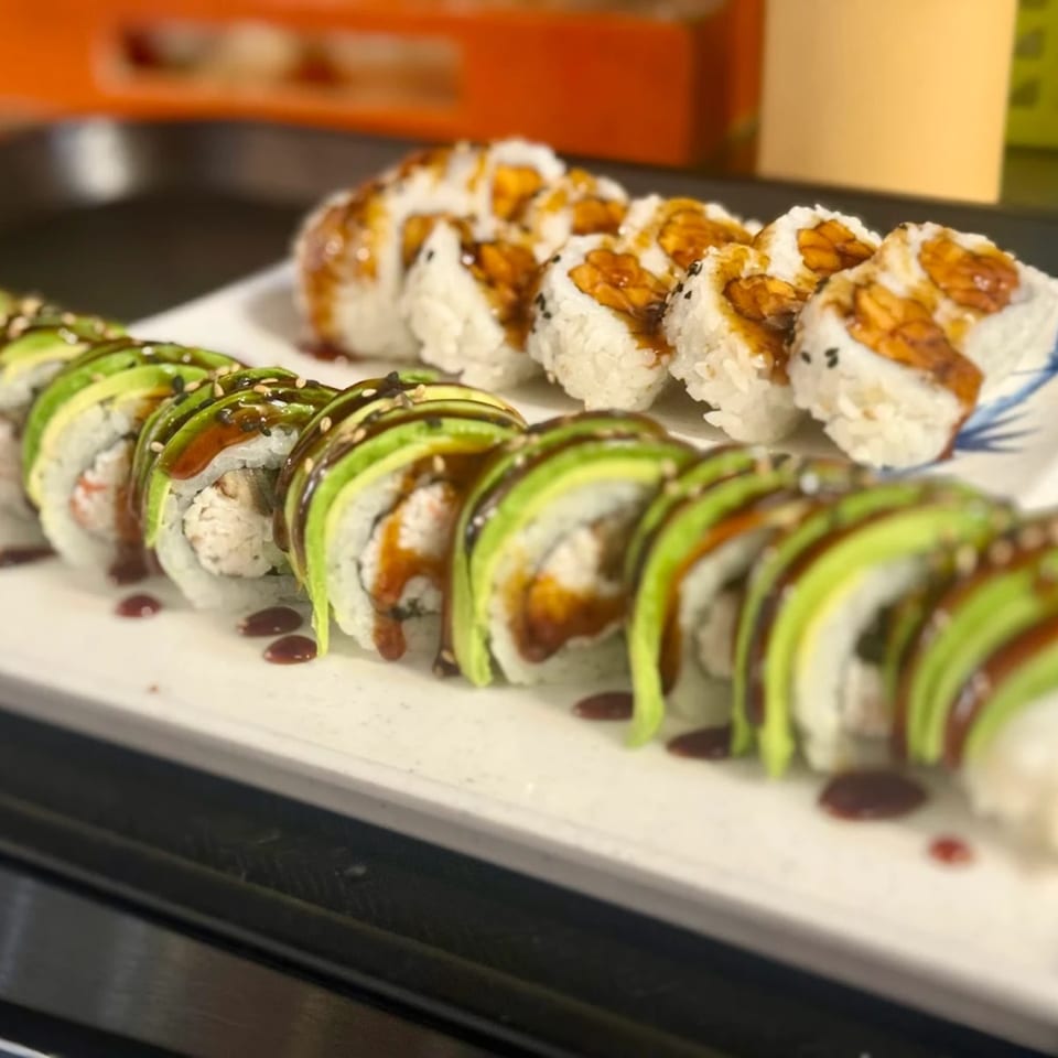 Two plates of Twin Sushi PDX rolls, one with avocado and sauce, the other with eel sauce.