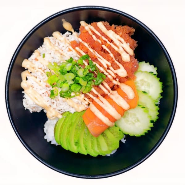Overhead view of a sushi bowl with rice, crab, spicy tuna, salmon, avocado, cucumber, and green onions.