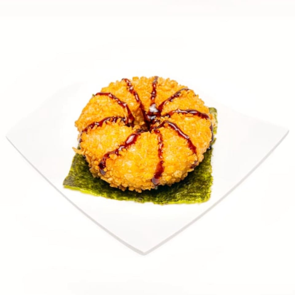 Deep-fried sushi donut drizzled with dark sauce, served on a nori sheet and white plate.