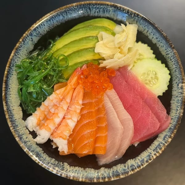 A colorful chirashi bowl with salmon, tuna, shrimp, avocado, seaweed salad, and roe.