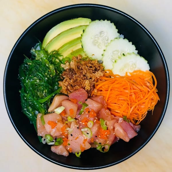 A colorful poke bowl with tuna, avocado, cucumber, seaweed, carrots, and crispy onions.